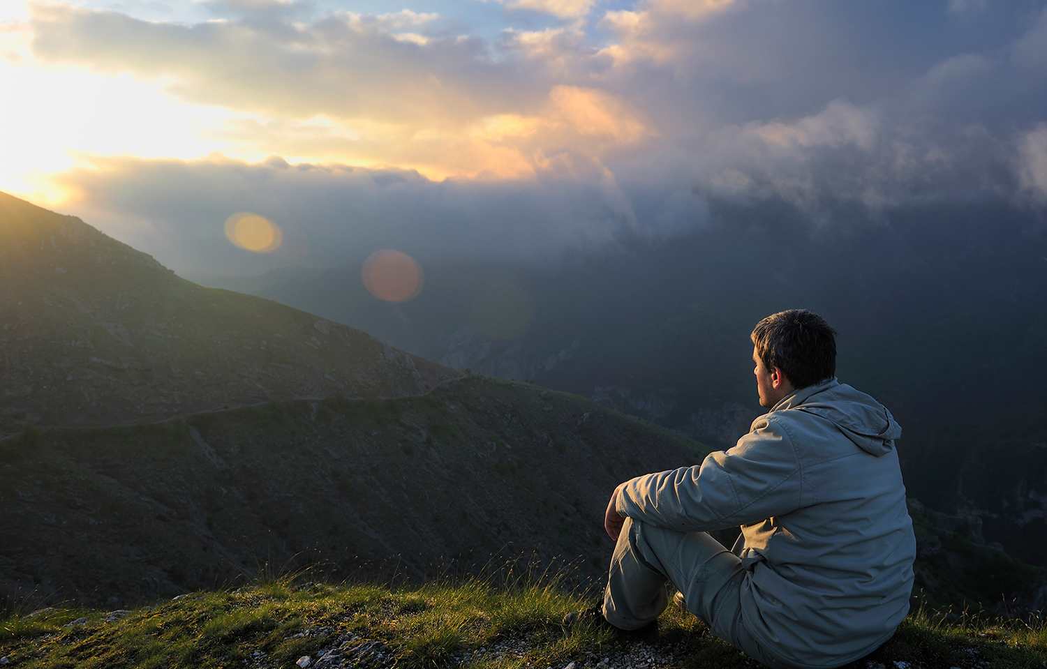 Man sitting on hillside looking at sunrise and vista
